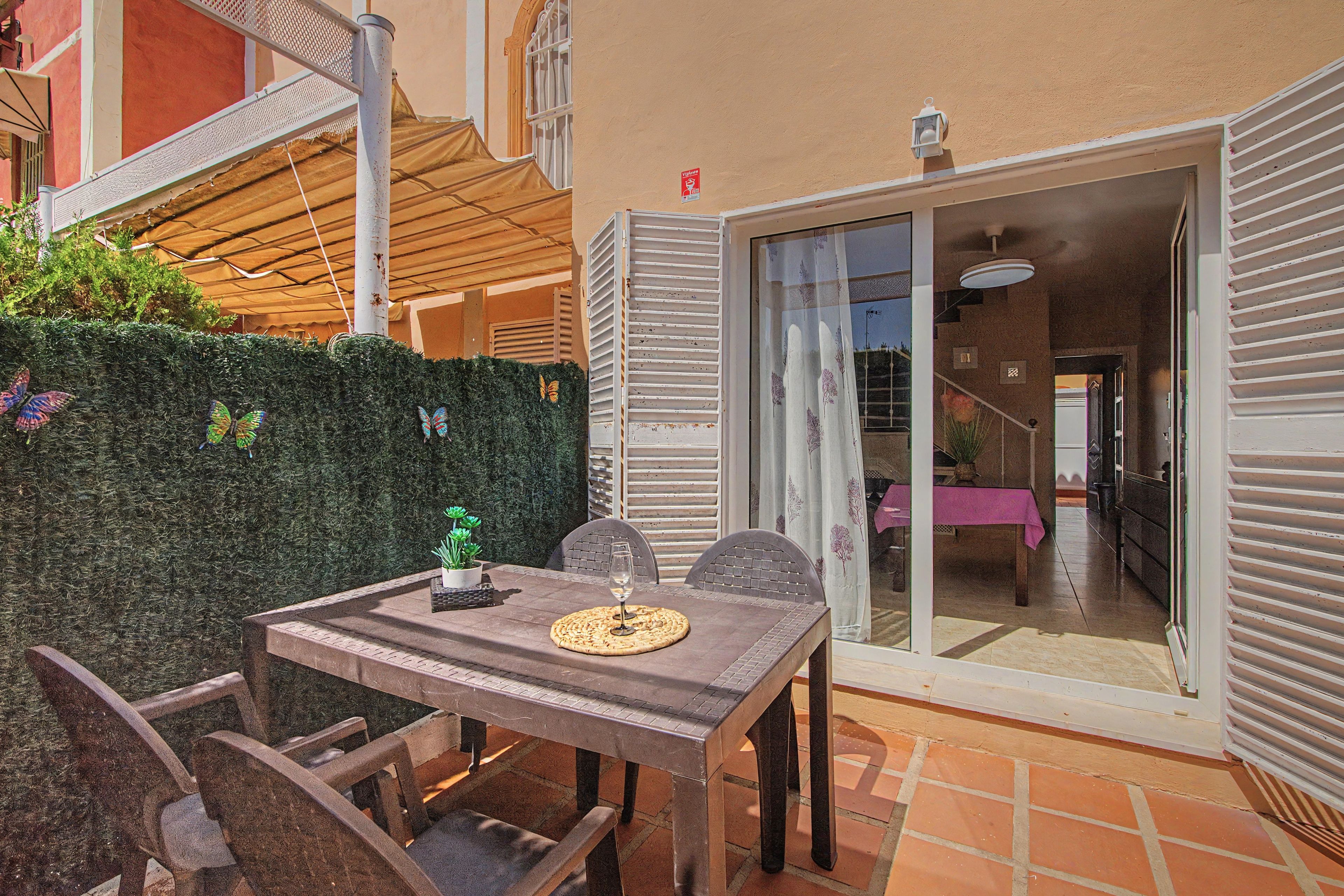 Un patio con una mesa, sillas, una planta en maceta y vista hacia el interior de la casa.