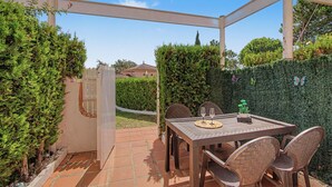 An outdoor patio with a table and chairs, surrounded by greenery and a fence.