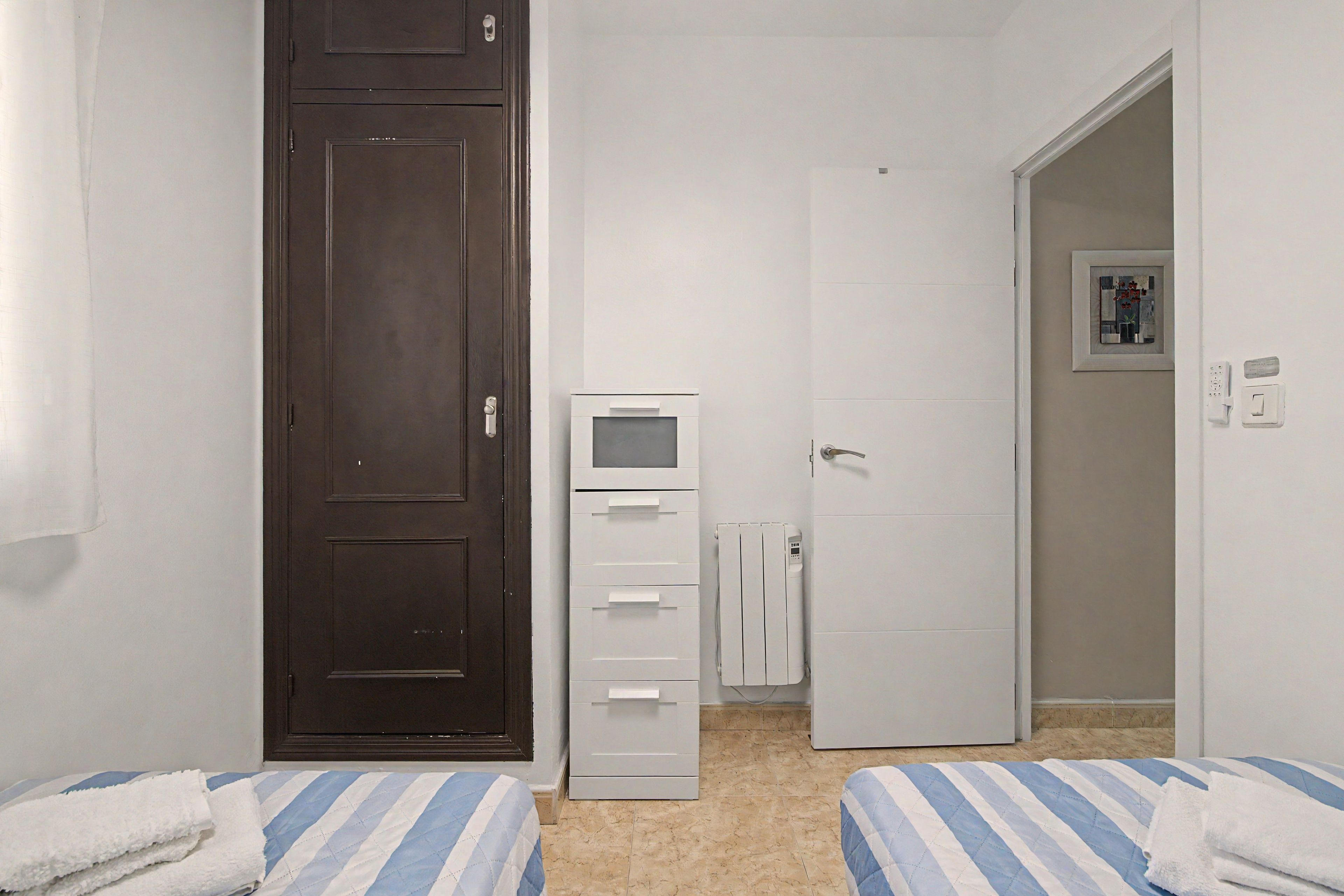 Ein Schlafzimmer mit zwei Betten, einer dunklen Tür, einem weißen Schrank und einer weißen Heizung.