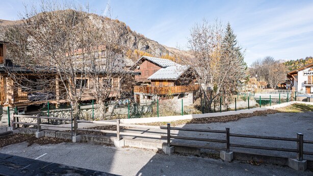 Ein traditionelles Holzhaus mit geneigtem Dach, umgeben von kahlen Bäumen und einer Bergkulisse.