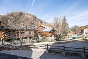 A traditional wooden building with a sloped roof, surrounded by bare trees and a mountainous backdrop.