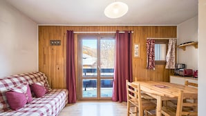 Ein Zimmer mit einer Holzwand, einem karierten Sofa mit Kissen, einem Holzesstisch mit Stühlen und einer Schiebetür zum Außenbereich.