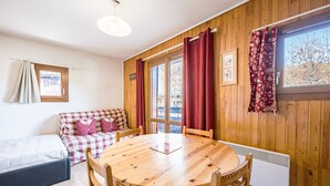 Ein gemütliches Zimmer mit Holzboden, einem karierten Sofa, einem runden Holztisch und einem Fenster mit Vorhängen.