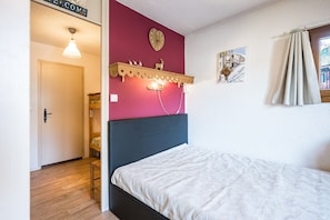 A bedroom with a bed, a wall-mounted shelf with a clock, a door, and a window with curtains.