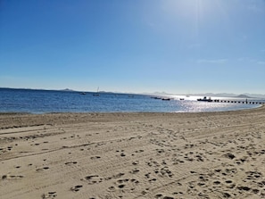 Ein Strand mit Fußabdrücken, einem klaren Himmel und Booten im Wasser.