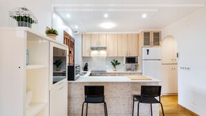 A modern kitchen with white cabinetry, a central island, two bar stools, and a built-in oven. - Villa 'Artep' with Shared Pool, Wi-Fi and Air Conditioning (Cartagena)
