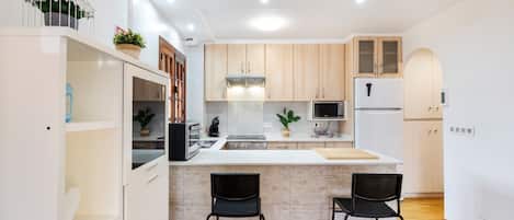 A modern kitchen with white cabinetry, a central island, two bar stools, and a built-in oven.
