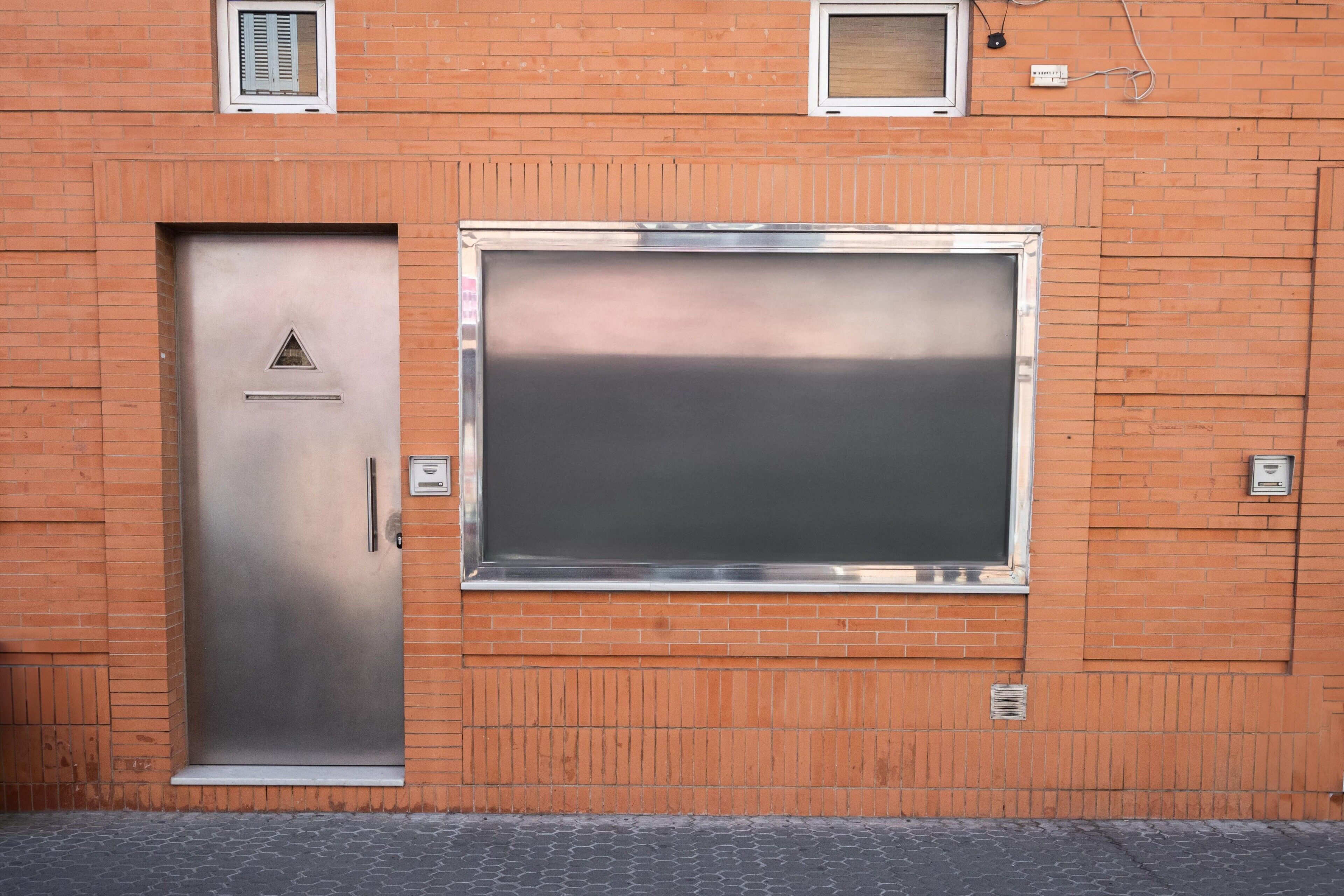 A metallic door with a triangular symbol, a large window, and a brick wall.