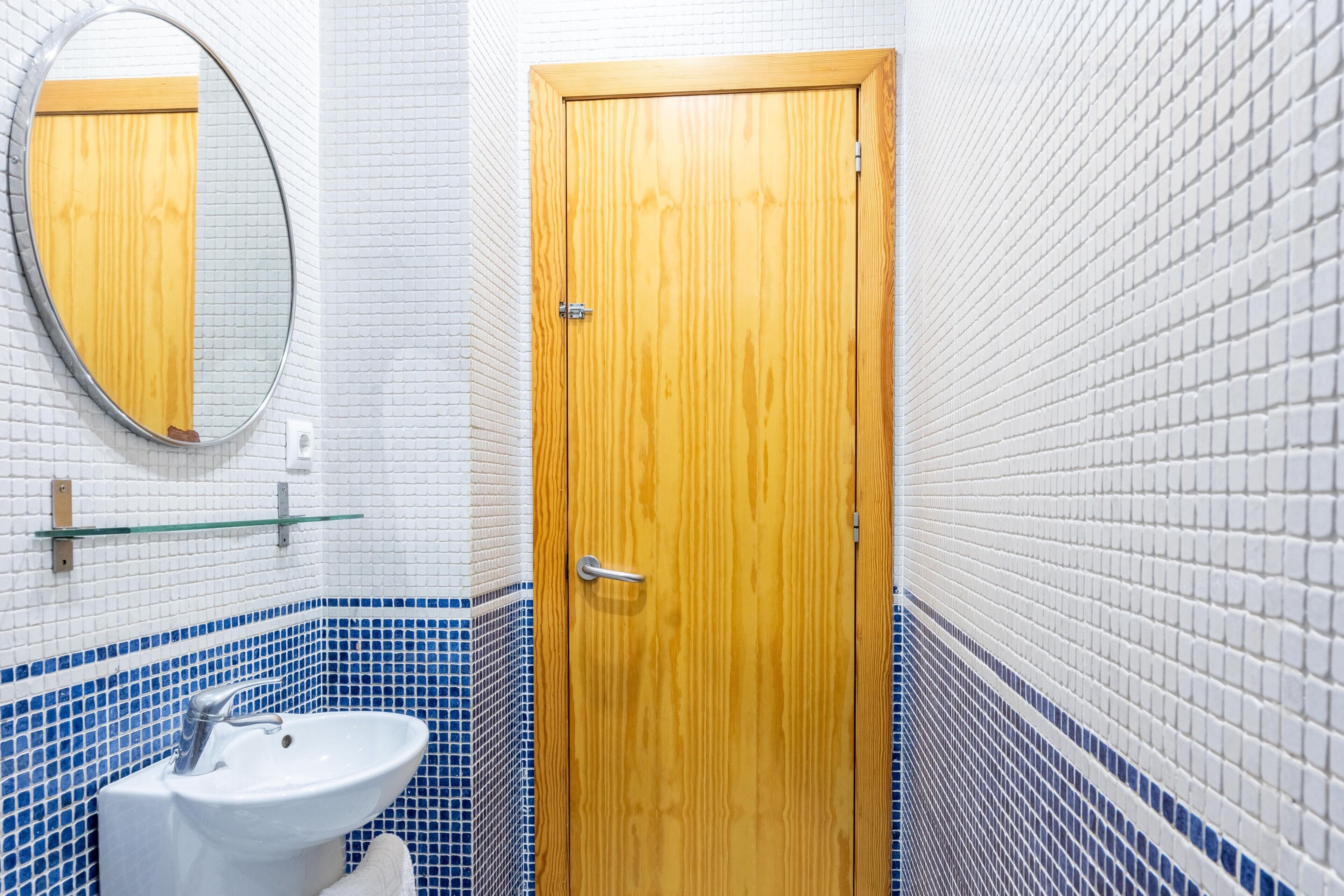 Un baño con puerta de madera, lavamanos blanco y espejo.