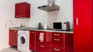 Una cocina funcional con lavadora, microondas y armarios rojos.