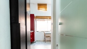 Un pasillo con una puerta, una ventana con persianas, una silla y un armario rojo.