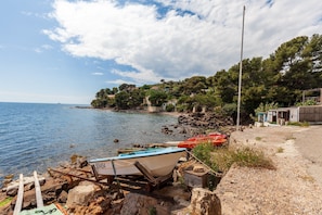 Paesaggio costiero con una barca su un rimorchio, una riva rocciosa e edifici sullo sfondo.