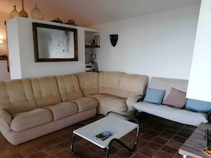 Un soggiorno con un divano componibile, un tavolino bianco e un letto con cuscini.