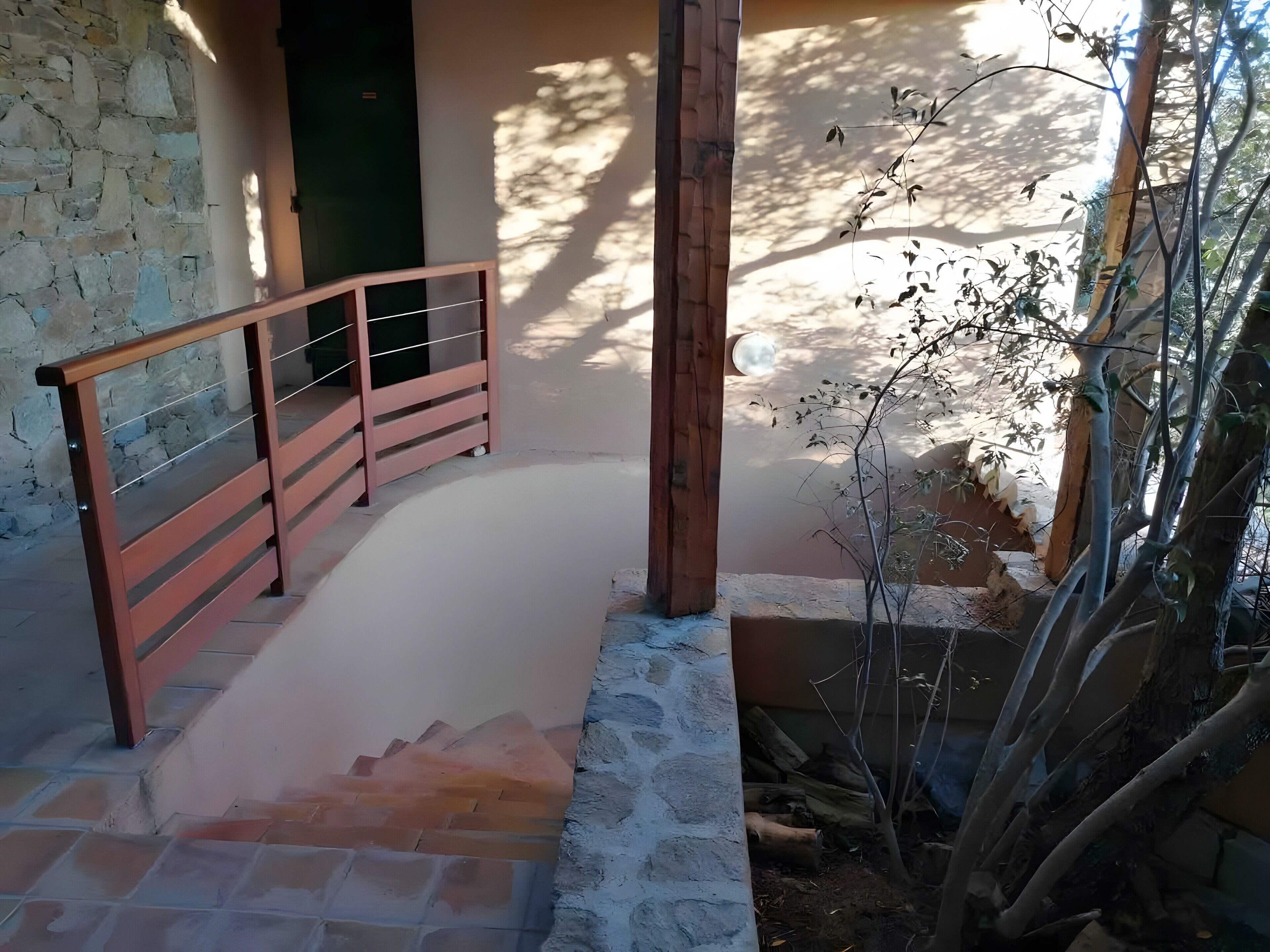Una escalera que lleva a un muro de piedra, una barandilla de madera y un árbol con ramas desnudas.
