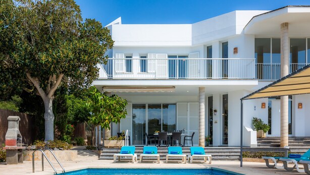 Una casa moderna de dos pisos con piscina, mobiliario exterior y un área de patio.