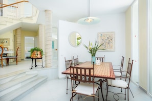 A dining area with a table, chairs, a vase with plants, a round mirror, and a staircase leading to an upper level.