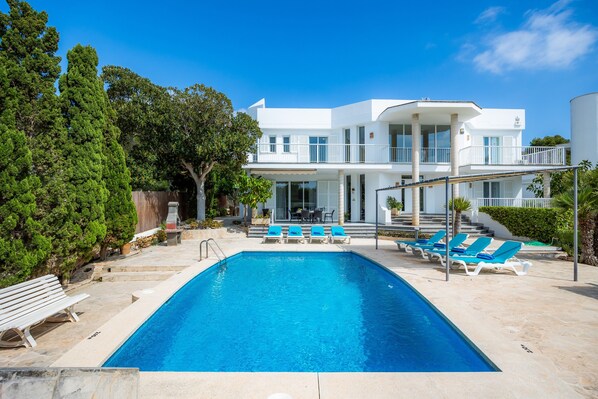 Una casa moderna de dos pisos con piscina, mobiliario de exterior y un jardín bien cuidado.
