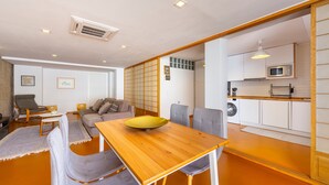 A modern living room with a wooden dining table, grey sofas, and a kitchen area with white cabinets and a microwave. - Apartment 'Casa Azahar' with Private Pool, Wi-Fi, and Air Conditioning (Níjar)