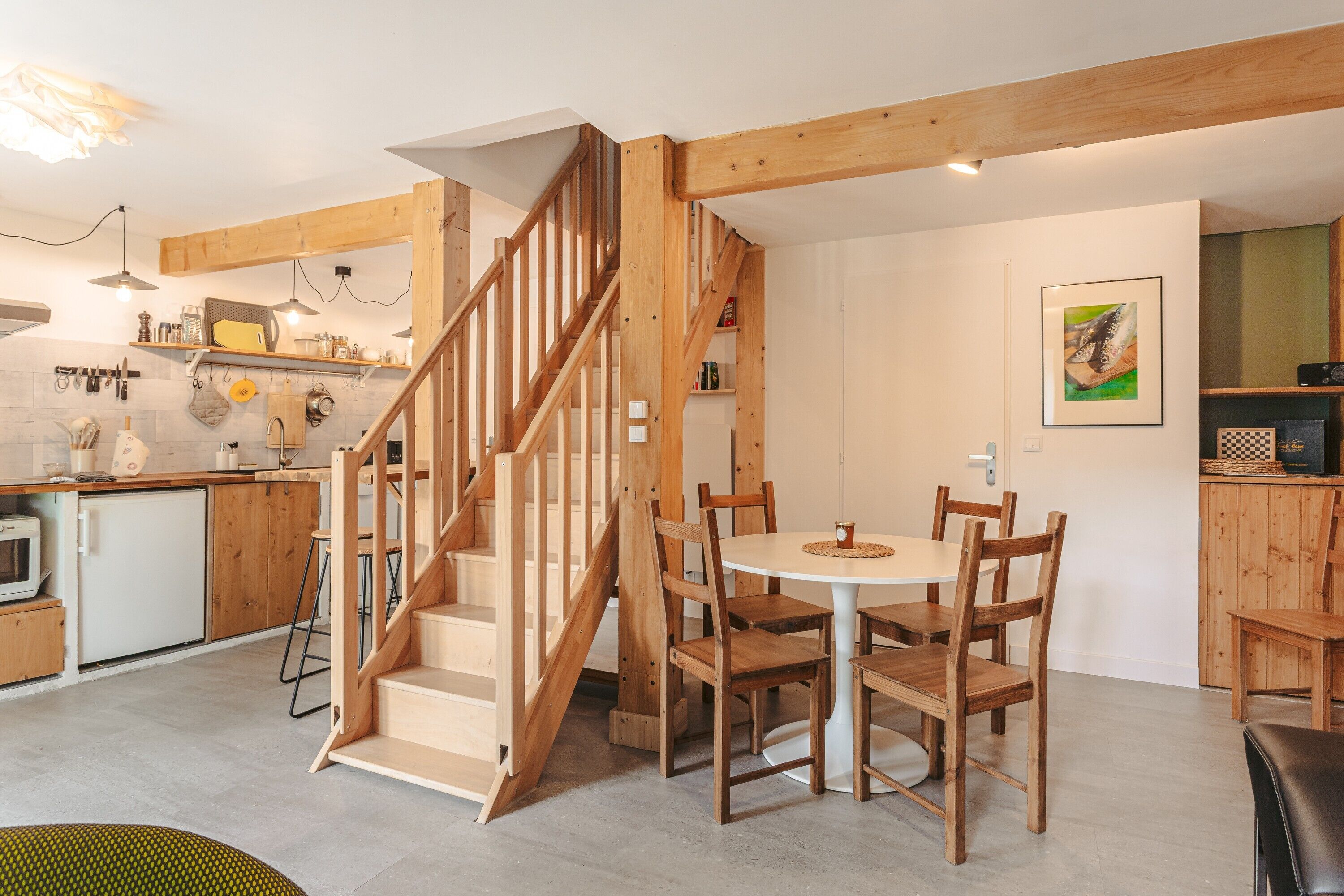 A modern kitchen with wooden beams, a dining area with a round table and chairs, and a staircase.