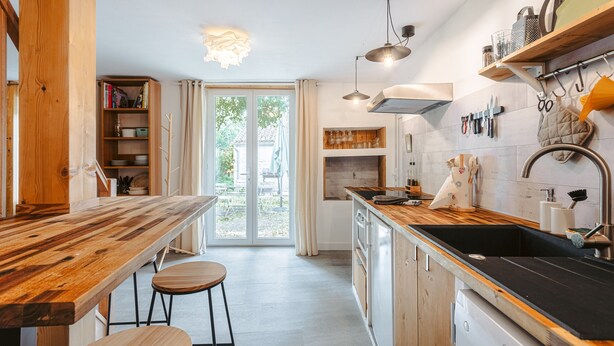 Een moderne keuken met een houten aanrecht, barstoelen, een inbouwvaatwasser en een groot raam.
