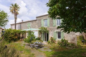 Ein Steinhaus mit Terrasse, Sitzgelegenheit im Freien und einer Palme.
