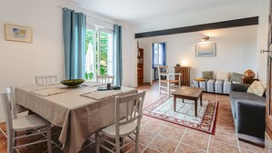 A dining area with a table and chairs, a sofa, a bookshelf, and a lamp. - Gabae - Les Volets Gris: Comfortable Holiday Home with Wi-Fi and Remote Work Space (Puyravault)