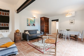 A living room with a sofa, a dining table, and a chair. There is a rug on the floor and a painting on the wall. - Gabae - Les Volets Gris: Comfortable Holiday Home with Wi-Fi and Remote Work Space (Puyravault)