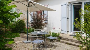 A patio with a table and chairs, a white building with a door, and a tree with red leaves. - Gabae - Les Volets Gris: Comfortable Holiday Home with Wi-Fi and Remote Work Space (Puyravault)