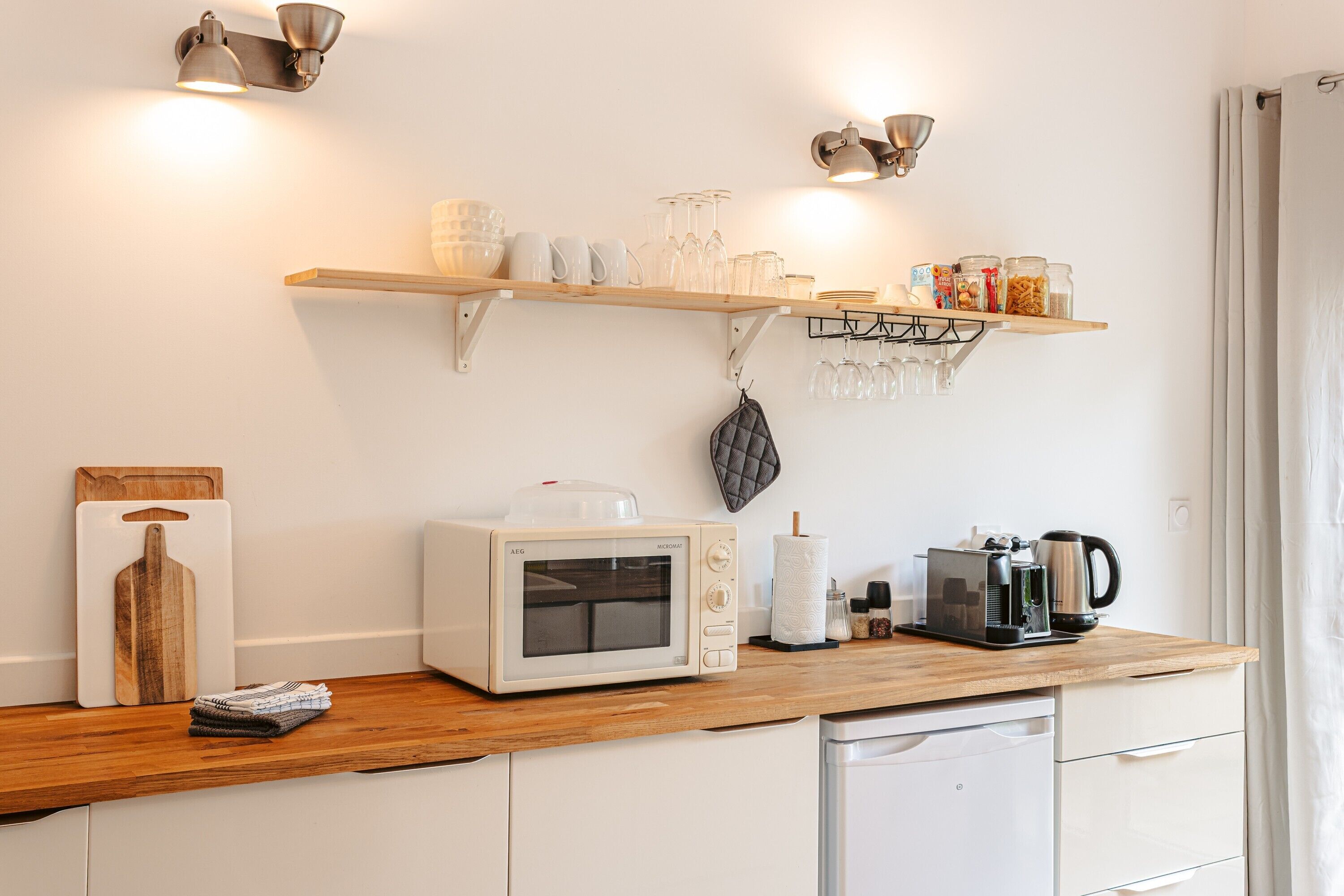 A kitchenette with a microwave, coffee maker, and shelf with glassware and jars.