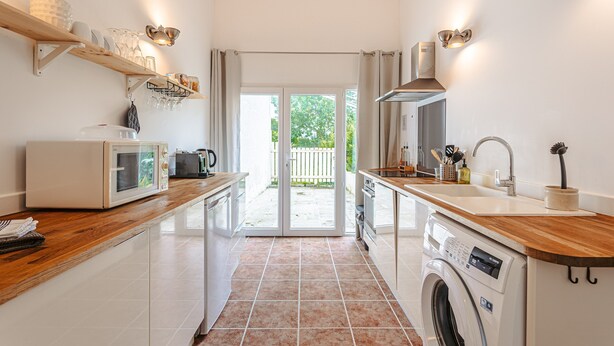 A modern kitchen with a microwave, oven, and washing machine, wooden countertops, and a view to the outside. - Gabae - Les Volets Gris: Comfortable Holiday Home with Wi-Fi and Remote Work Space (Puyravault)