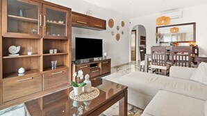 A living room with a TV, wooden cabinets, a glass coffee table, and a dining area with chairs and a table. - Apartment 'Top Floor Fuengirola Park' with Private Terrace, Wi-Fi and Air Conditioning (Fuengirola)