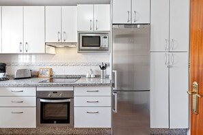 Une cuisine moderne avec des meubles blancs, un four à micro-ondes, un réfrigérateur, un grille-pain et un four.