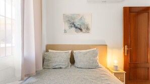 A bedroom with a bed, a nightstand with a lamp, a wooden door, and a wall-mounted air conditioner. - Apartment 'Top Floor Fuengirola Park' with Private Terrace, Wi-Fi and Air Conditioning (Fuengirola)