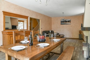 A dining area with a wooden table set for four, a sofa, and a painting on the wall. - Holiday Home 'Le Moulin De Bayard' with Mountain View, Private Terrace & Wi-Fi (Pontcharra)