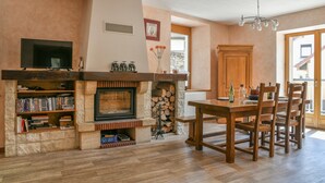 Un salon avec une cheminée, des étagères à livres, une table à manger avec des chaises et un téléviseur fixé au mur.