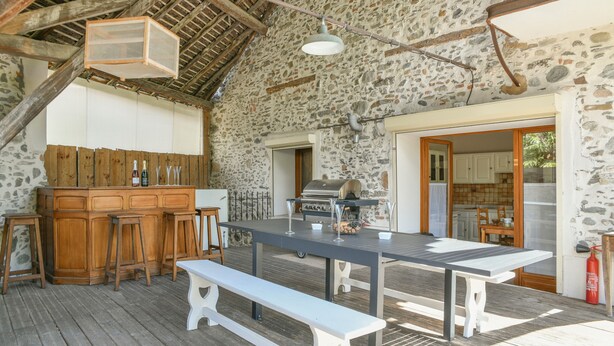Un espace extérieur aménagé pour les repas, avec un mur en pierre, un bar en bois et un barbecue.