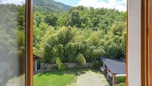 Une vue à travers une fenêtre sur un paysage verdoyant luxuriant, avec une montagne en arrière-plan, un espace extérieur abrité et un bâtiment doté d’un toit en pente.