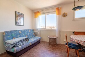 Una habitación con sofá, una mesa, una silla de mimbre, una ventana con cortinas, un reloj de pared y un cuadro enmarcado.