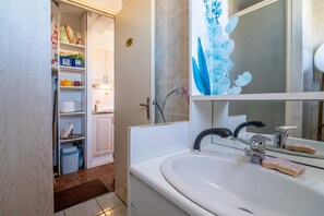 Un baño con un lavamanos blanco, un espejo y una repisa con artículos de tocador.