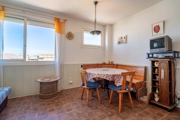 Una habitación con una mesa de comedor, sillas, un televisor, un armario y una ventana con cortinas.