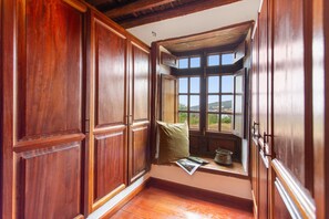 A room with wooden paneling, a window with a view, and a small window seat with a cushion and a metal pot.