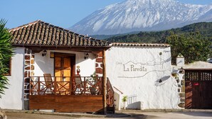 A building with a tiled roof, a wooden porch with chairs, and a mountain in the background. - Vacation 'Casa Guimar' with Sea View, Wi-Fi and Air Conditioning (Tanque)