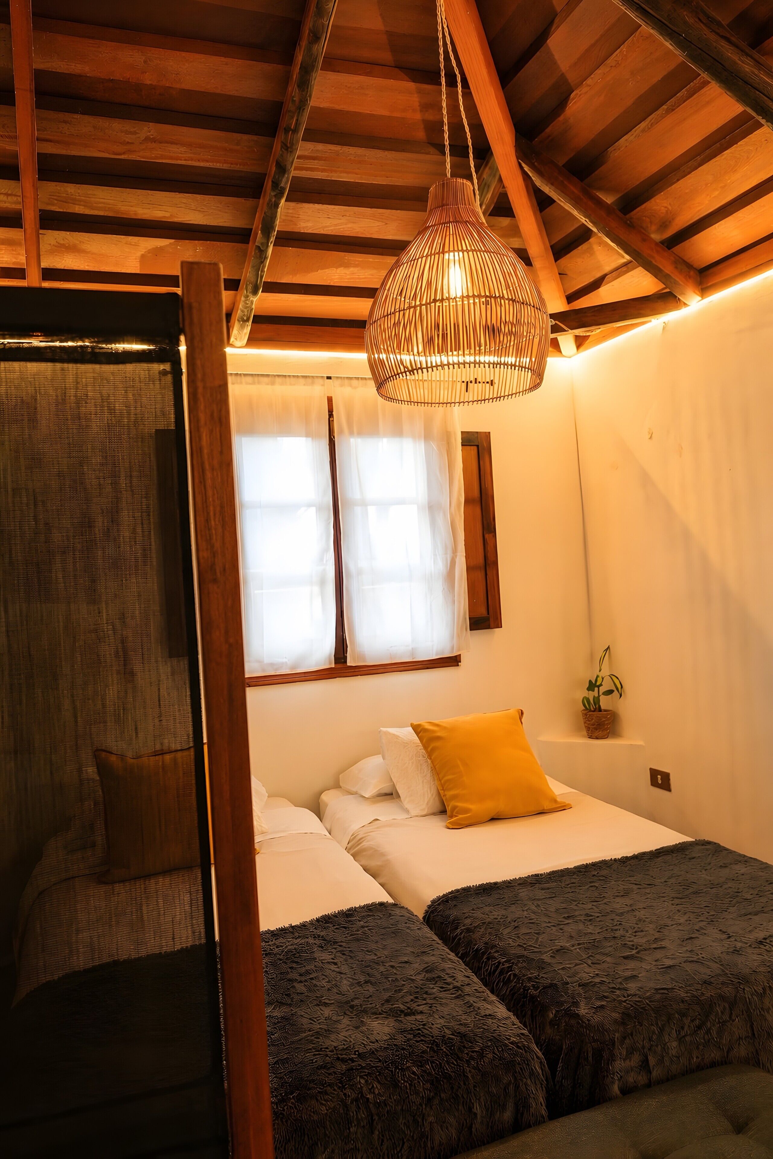 A bedroom with a bed, two bedside tables, a hanging light fixture, and a window with curtains.