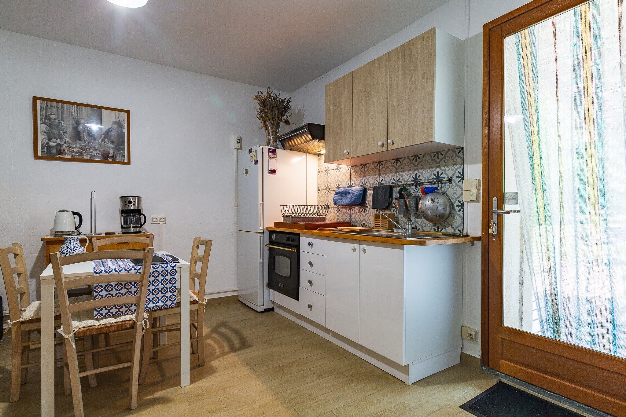 Cocina compacta con armarios de madera, salpicadero de azulejos y comedor con mesa y sillas.