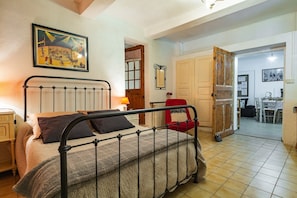A bedroom with a metal bed frame, a wooden door, a dining area with a table and chairs, and a framed picture on the wall.