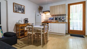 Kompakti keittiö, jossa on ruokapöytä, tuolit, kahvinkeitin ja jääkaappi.