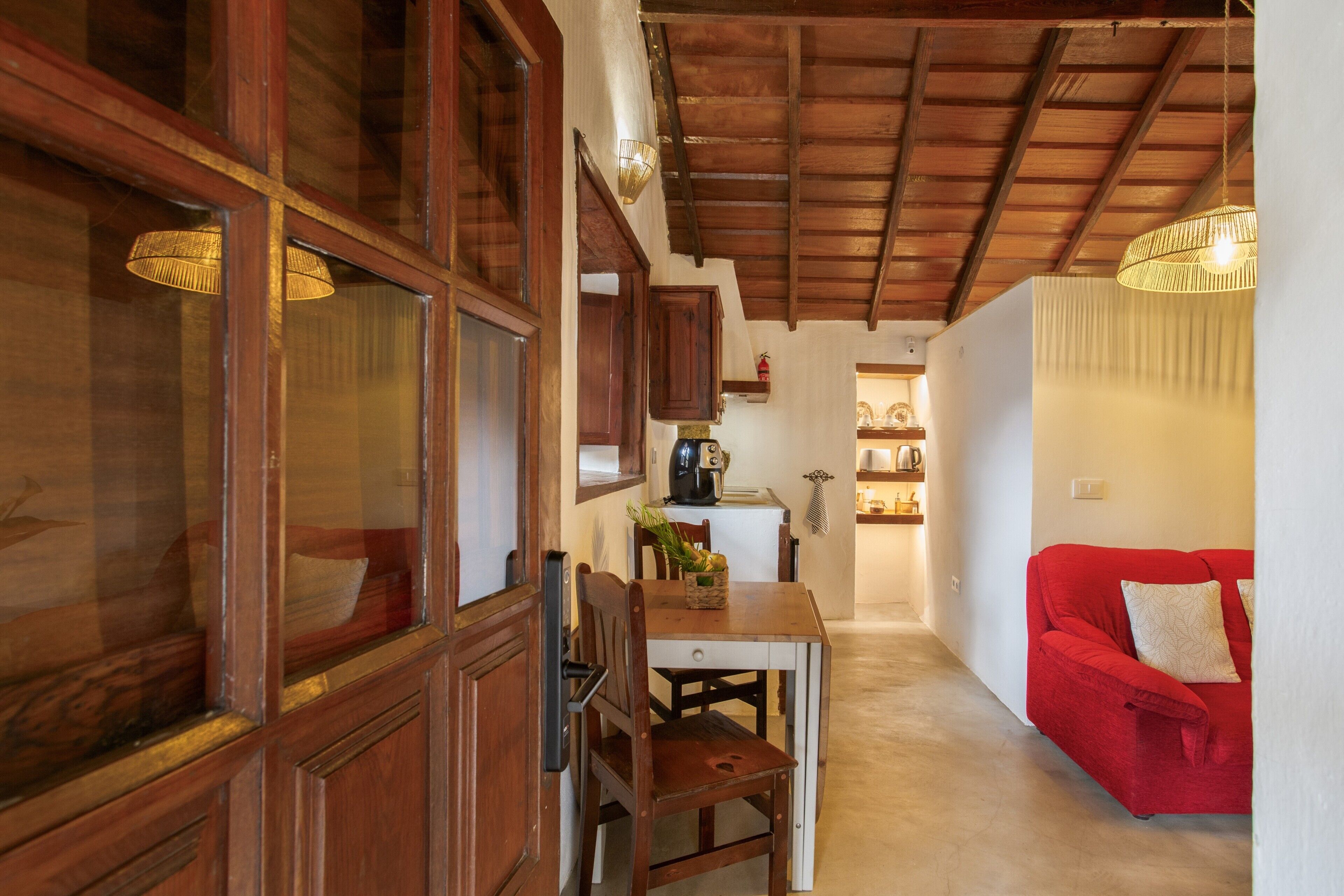 A wooden dining table with chairs, a red sofa, and a kitchen area in the background.