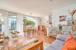 A spacious living area with a sofa, coffee table, and chairs, a dining set, and a bookshelf.