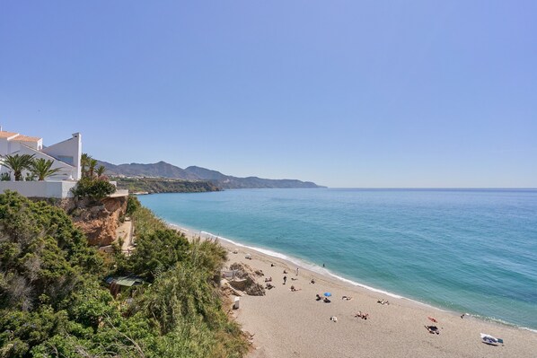 A beach with a clear view of the sea, a few people, and a building with a white facade.