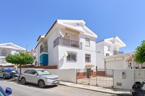 Un edificio residencial de dos plantas con balcón, antena parabólica y entrada protegida por una reja.